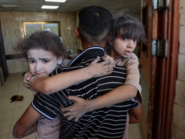 A Palestinian carries children as wounded Palestinians receive treatment at Al-Aqsa Martyrs Hospital, after an Israeli airstrike on a house, in Deir al-Balah, central Gaza Strip, July 8, 2025. REUTERS/Ramadan Abed