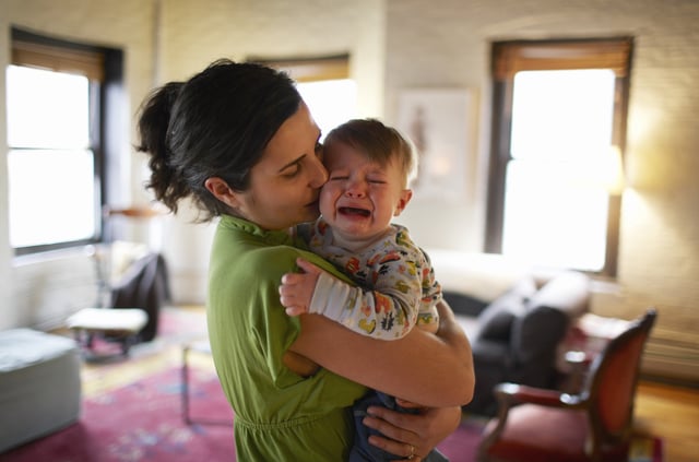 Mother holding and kissing crying baby boy.