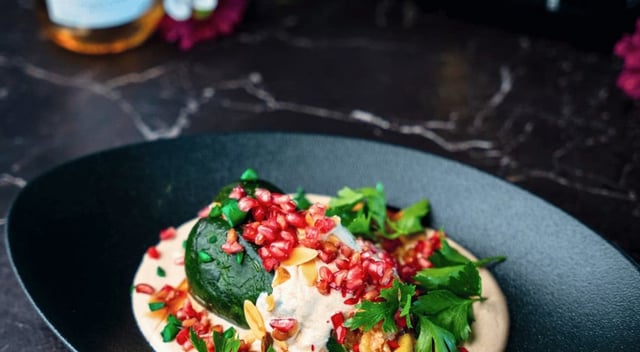 Plato de chile en nogada típico de Puebla, servido con nogada cremosa, granada fresca, hojas de perejil y almendras fileteadas sobre un plato de cerámica negra. Este platillo representa uno de los íconos de la cocina mexicana y es protagonista de la temporada gastronómica 2025 en Puebla. Fotografía: Cuartoscuro / Isabel Mateos