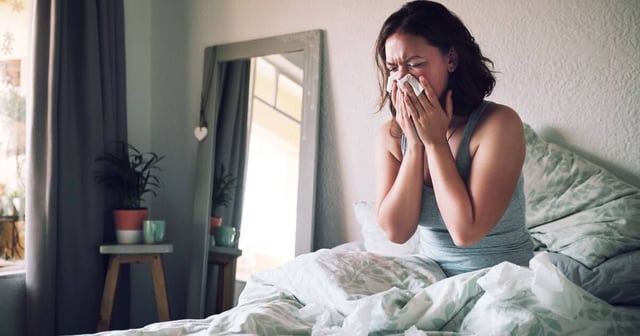 A young woman sits sick in bed. Shuttertock