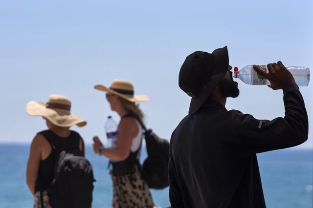 FILE - A tourist drinks water on a hot day at the beach in Barcelona, Spain, July 2, 2025. (AP Photo/Emilio Morenatti, File)