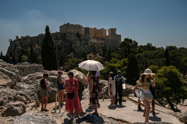 Des touristes se protègent du soleil en face de la colline de l'Acropole à Athènes, le 8 juillet 2025 en Grèce
