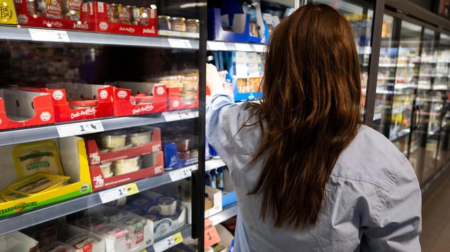 Eine Frau greift nach einem Lebensmittel an einem Kühlregal eines Supermarkts. 