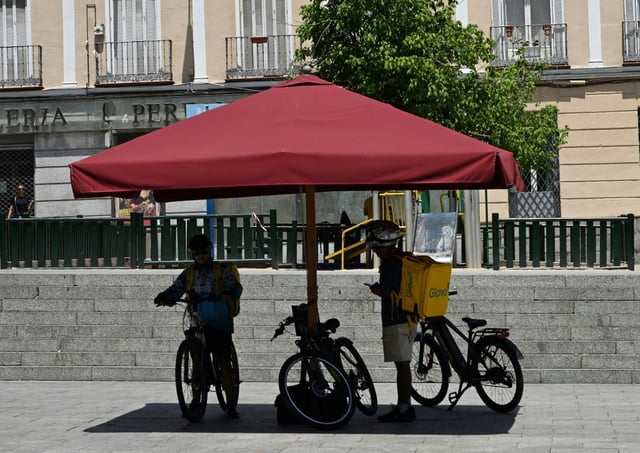 Des livreurs s'abritent du soleil sous un parasol à Madrid, le 18 juin 2025 lors d'une vague de chaleur en Espagne