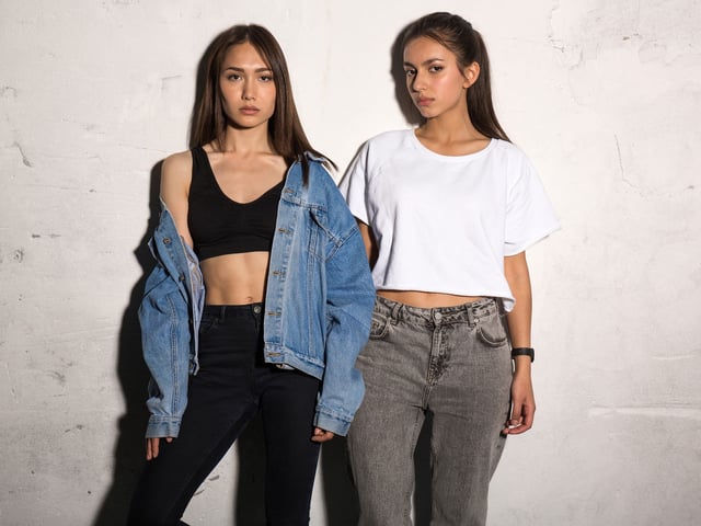 Picture of concentrated young hipsters ladies standing over gray background.
