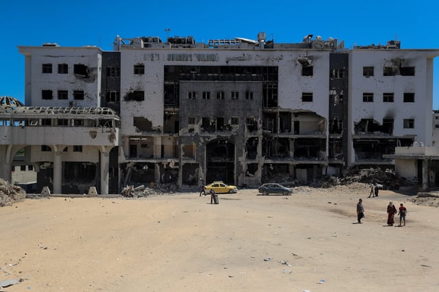 Palestinians walk next to a damaged building at Al-Shifa hospital, which Gaza's health ministry says is at risk of shutting down due to the Israeli blockade of fuel, in Gaza City July 9, 2025. REUTERS/Mahmoud Issa