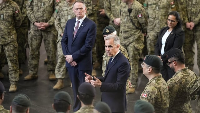 Prime Minister Mark Carney stands with Minister of National Defence David McGuinty as he talks to service personnel following an announcement at Fort York Armoury in Toronto on Monday June 9, 2025. THE CANADIAN PRESS/Chris Young