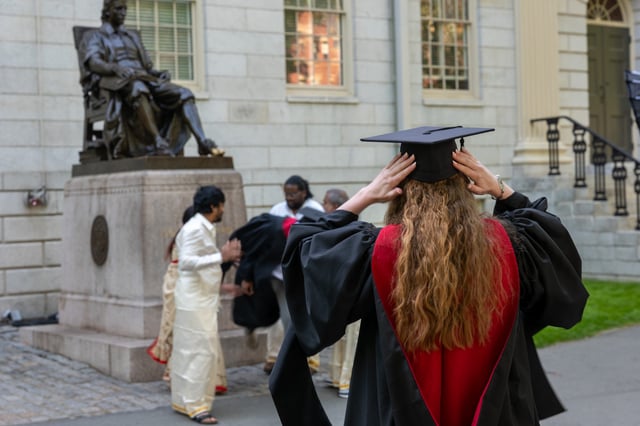 Graduation students, faculty, and family gather in front of the statue of John Harvard in Harvard Yard on May 28, 2025 in Cambridge, Massachusetts.