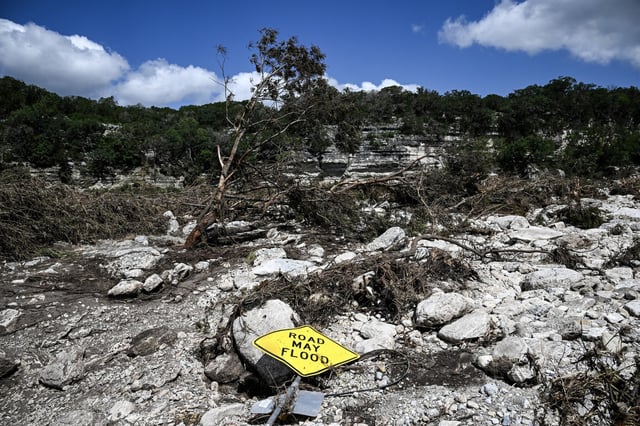 A traffic sign reading "Road may flood" lies on the ground near the Guadalupe River in Hunt, Texas, on July 8, 2025.