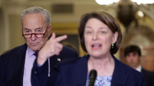 Senate Minority Leader Chuck Schumer listens behind Sen. Amy Klobuchar. Photo: Alex Wong/Getty Images