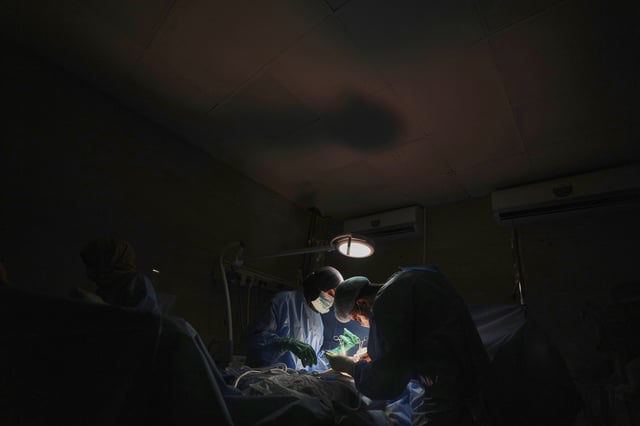 Dr. Abeer Al-Gharbawi, left, performs surgery under the illumination of a battery-powered light during a power outage at Shifa Hospital in Gaza City, Friday, July 4, 2025. (AP Photo/Jehad Alshrafi)