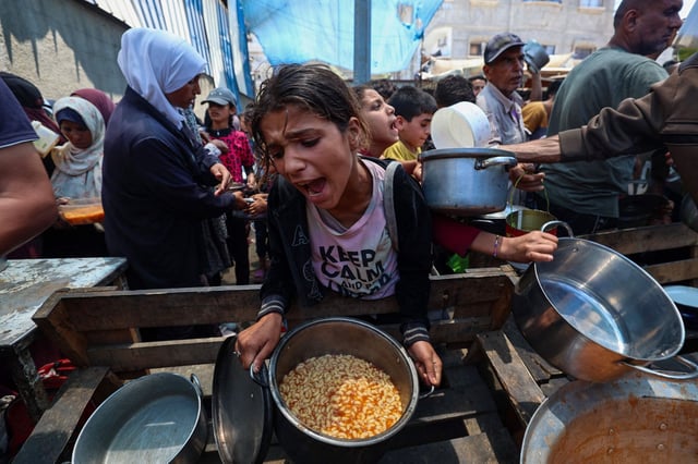 Una niña reacciona tras recibir comida preparada mientras otras esperan en un punto de distribución en Nuseirat, en el centro de la Franja de Gaza, el 2 de junio de 2025.