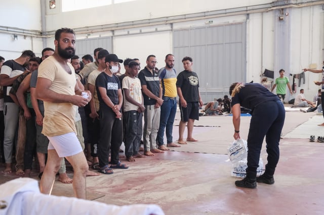 A Greek coast guard gives water to migrants from Africa as they take a shelter in Agia port, Chania, Crete island, Greece, Monday, July 7, 2025. (AP Photo/Giannis Angelakis)
