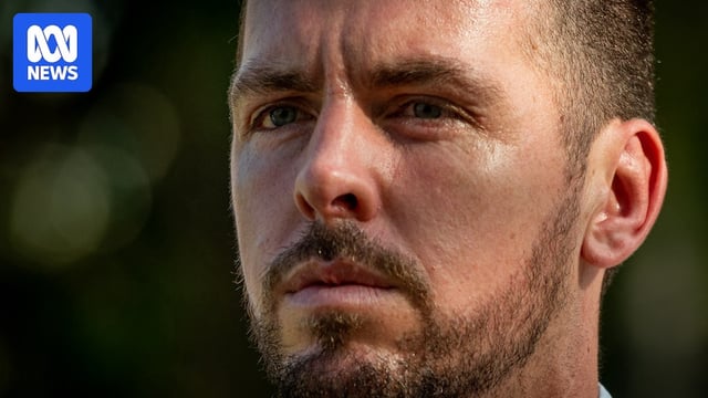 A tight close-up of a white man with a beard and moustache - Zacahary Rolfe - with a stern expression, frowning.