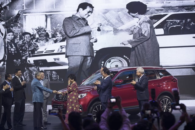 FILE - Malaysia Prime Minister Mahathir Mohamad, left, hands the keys to his wife Siti Hasmah as it is shown on the screen when he launched the first Proton car 35 years ago during the launch of Proton new SUV in Kuala Lumpur, Malaysia, Dec. 12, 2018. (AP Photo/Vincent Thian,File)