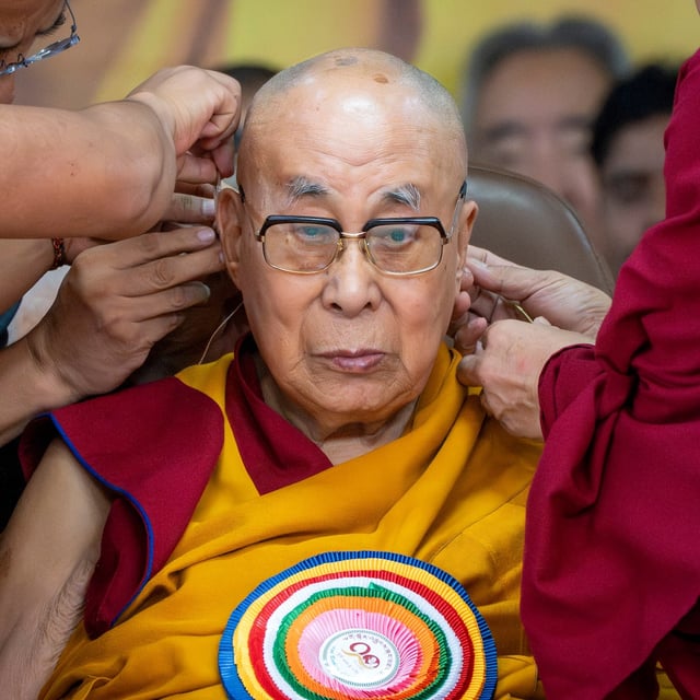 Attendant monks help put a microphone around Tibetan spiritual leader the Dalai Lama's head during his 90th birthday celebrations at the Tsuglakhang temple in Dharamshala, India, Sunday, July 6, 2025.(AP Photo/Ashwini Bhatia)
