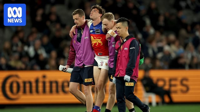 A Brisbane Lions player grimaces as he is helped off the field by a number of medical officials.