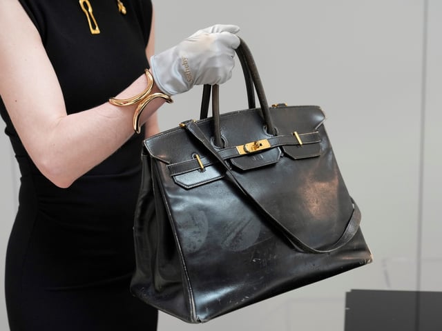An auction officer carries the original Birkin bag created by Hermès for Jane Birkin in 1984, prior to its auction Thursday, July 10, 2025 in Paris. (AP Photo/Michel Euler)
