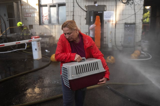 A woman carrying a cat in a pet carrier makes her way past fire hoses as she leaves a shelter following a major overnight Russian attack in Kyiv on July 10, 2025, amid the Russian invasion of Ukraine. 