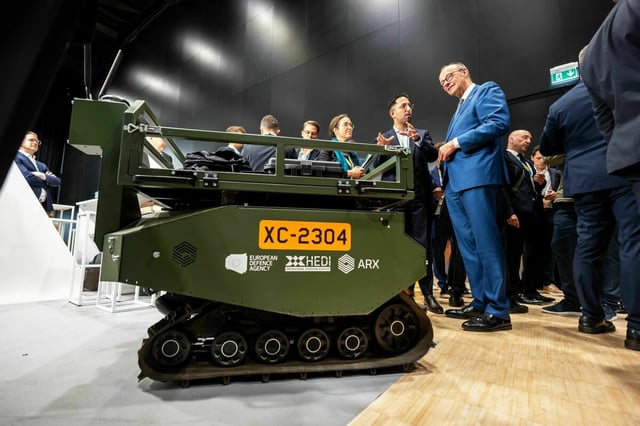 Friedrich Merz lässt sich ein ferngesteuertes Transportfahrzeug bei der Wiederaufbaukonferenz für die Ukraine erklären