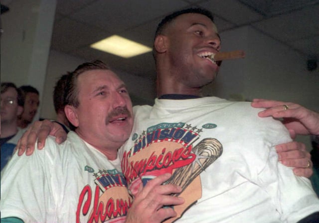 Ken Griffey Jr. (R) of the Seattle Mariners has a celebratory cigar and embraces batting coach Lee Elia during a victory party in the locker room after the Mariners 9-2 win over the California Angels on Oct. 2, 1995 in Seattle.