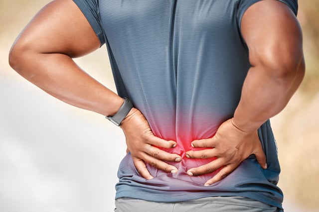 A stock image shows a man standing alone, suffering from low back pain.