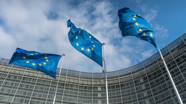 European Union flags wave outside the European Commission building in Brussels, where officials unveiled a new code of practice on general-purpose AI. The voluntary guidelines aim to enforce transparency, copyright protections, and safety standards for advanced AI systems like ChatGPT.