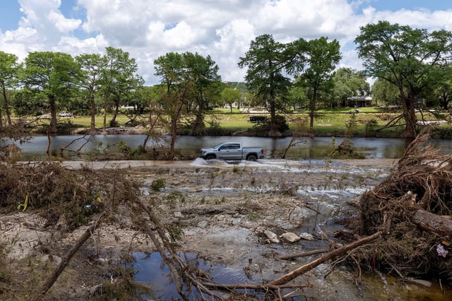 A vehicle drives through a road flooded by the waters of the Guadalupe River in Hunt, Texas, on July 9.