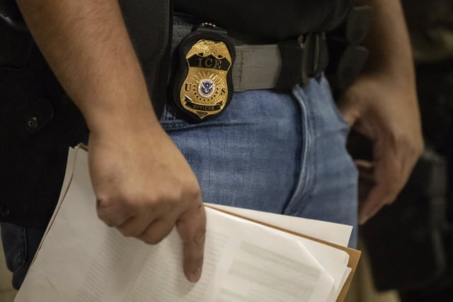 A federal agent wears a badge of Immigration and Customs Enforcement while standing outside an immigration courtroom at the Jacob K. Javits Federal Building in New York, Tuesday, June 10, 2025.
