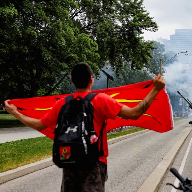 A demonstrator, standing next to a police officer, holds a flag during a protest in front of the Legislative Assembly of Ontario against the federal government’s Bill C-5, as members of the Canadian Armed Forces fire cannons in the background during a celebration marking Canada Day, in Toronto, Ontario, Canada, July 1, 2025. REUTERS/Wa Lone