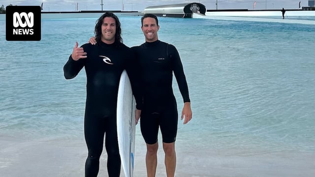 Two men in wetsuits stand together near water