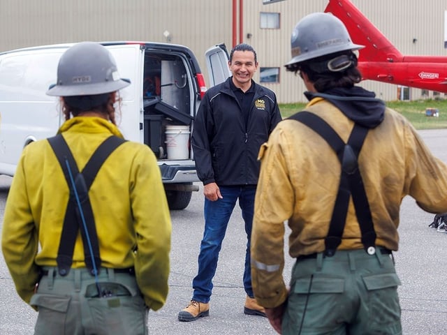 Manitoba Premier Wab Kinew chats with members of the Logan Hotshots from the U.S. Forest Service as they prepare to drop into a wildfire hot zone for the day in the surrounding area of Flin Flon, Man. on June 12, 2025.