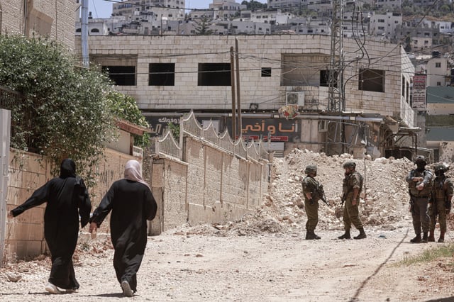 Palestinian women carry their belongings as Israeli soldiers enforce an evacuation order on a house in the Jenin refugee camp in the Israeli occupied West Bank on July 8, 2025.