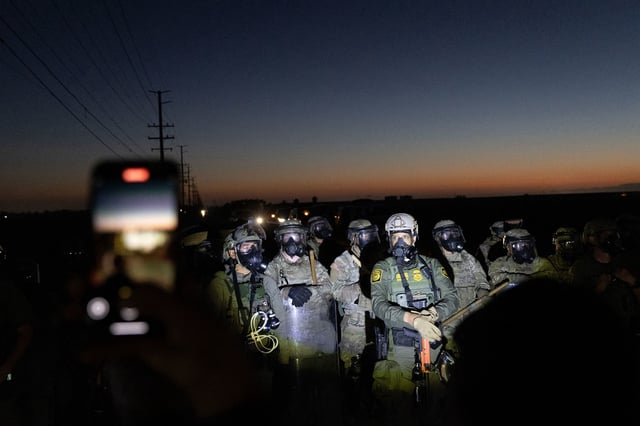Customs and Border Protection officers and California National Guard troops hold the line as protestors shine flashlights on them after Federal Immigration agents conducted a raid on Glass House Farms in Camarillo, California, on July 10, 2025. Federal immigration agentsbacked by CBP, Border Patrol units, National Guard troops, helicopters, and military style vehiclesraided Glass House Farms in Camarillo early July 10, 2025, targeting state licensed cannabis and other crop operations, detaining between a dozen and 100 farmworkers, and deploying smoke or tear gas canisters and rubber bullets to disperse a crowd of several hundred protesters on Laguna Road. (Photo by BLAKE FAGAN / AFP) (Photo by BLAKE FAGAN/AFP via Getty Images)          
