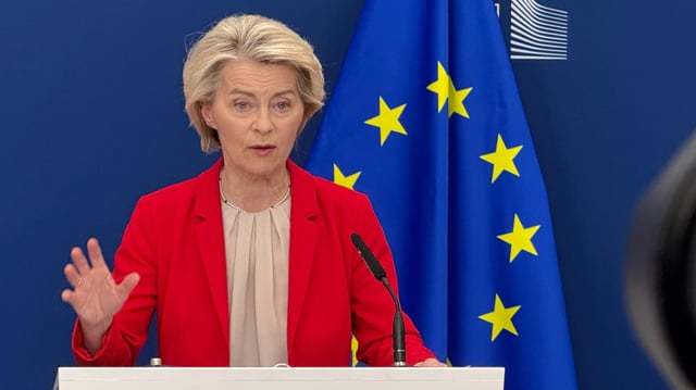 Ursula von der Leyen steht hinter einem rednerpult, im Hintergrund ist eine EU-Flagge zu sehen.