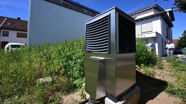  Vor einem neu gebauten Wohngebäude ist im Garten eine Wärmepumpe zum Heizen des Gebäudes in Betrieb.