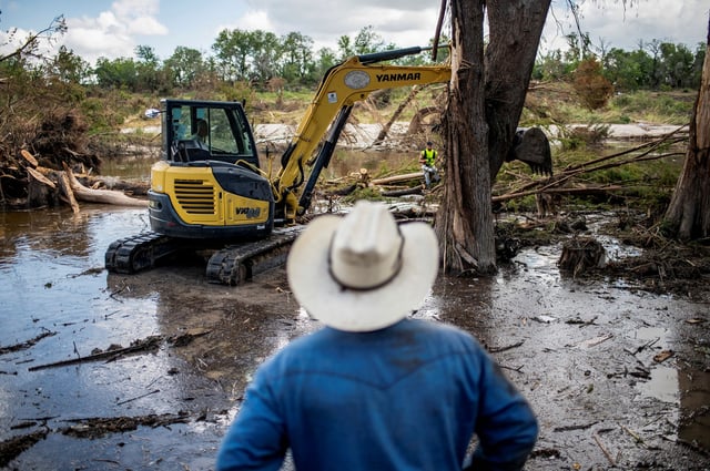 A person watches as machinery is used to clear debris along the banks of the Guadalupe River after catastrophic floods in Center Point, Texas, U.S., July 11, 2025.