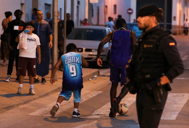 People play with a soccer ball as a police officer keeps watch, amid anti-migrant unrest following an attack on an elderly man by unknown assailants earlier in the week, in Torre Pacheco, Spain, July 13, 2025. REUTERS/Violeta Santos Moura