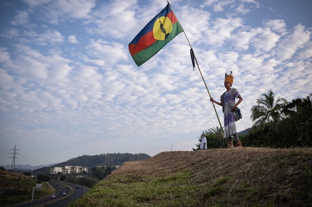 Une femme en tenue traditionnelle tient un drapeau kanak, dans le quartier de Dumbea, à Nouméa, en Nouvelle-Calédonie, en septembre 2024.