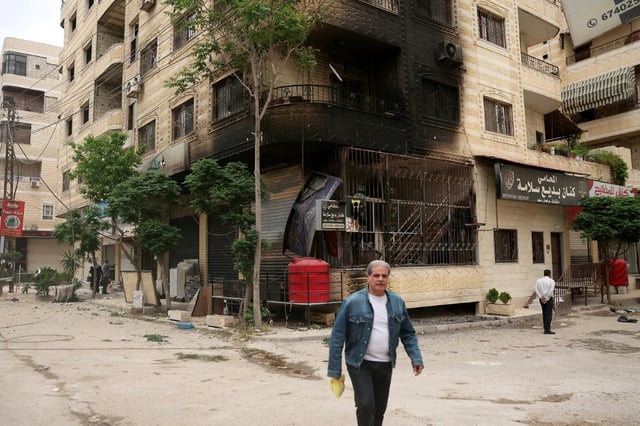 Un homme passe devant un bâtiment partiellement incendié lors de violences impliquant des druzes près de Damas, le 1er mai 2025