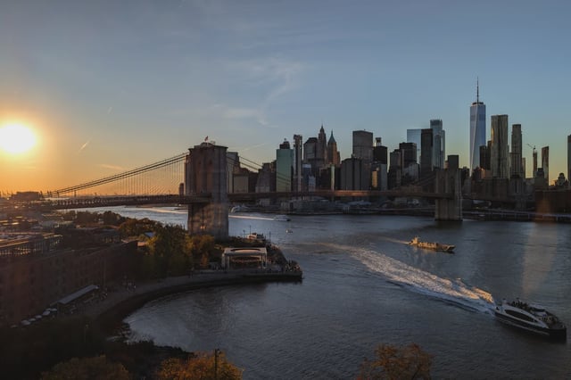 An NYC Ferry sails in the East River in front of the Brooklyn Bridge and lower Manhattan.