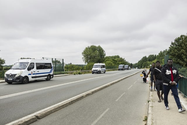 Un véhicule de police passe à coté de migrants qui quittent un camps de fortune après une opération de démantèlement des policiers à Dunkerque le 25 juin 2025