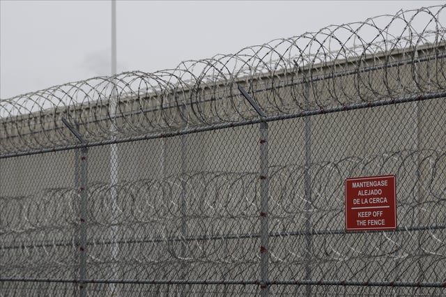FILE - Barbed wire fencing is shown behind a sign in English and Spanish in a recreation yard used by detainees during a media tour of the U.S. Immigration and Customs Enforcement detention center, Dec. 16, 2019, in Tacoma, Wash. (AP Photo/Ted S. Warren, file)