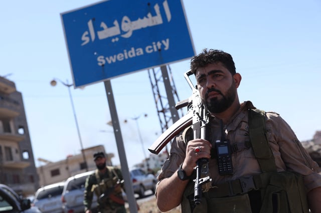 Un miembro de las fuerzas de seguridad sirias se encuentra bajo un cartel en la ciudad predominantemente drusa de Sweida, el 15 de julio de 2025