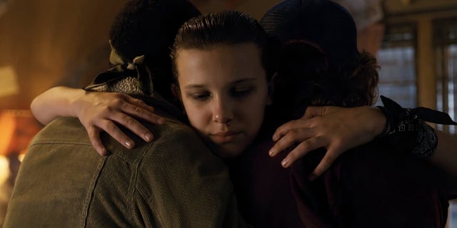 Millie Bobby Brown as Eleven in Stranger Things hugging Lucas and Dustin