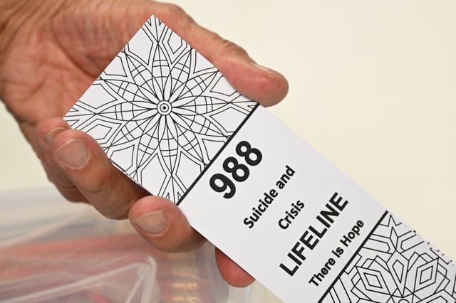 A bookmark for children with the 988 suicide and crisis lifeline emergency telephone number is displayed by Lance Neiberger, a volunteer with the Natrona County Suicide Prevention Task Force, while they speak about mental health and suicide awareness in Casper, Wyoming on August 14, 2022. Sixteen years ago, after his son died by suicide, Lance Neiberger thought of taking his own life.
Instead, the petroleum engineer — who lives in central Wyoming — is spearheading the difficult battle to curb the western US state’s suicide rate, the highest in the nation. (Photo by Patrick T. FALLON / AFP) (Photo by PATRICK T. FALLON/AFP via Getty Images)