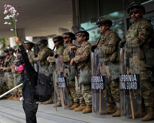 A demonstrator raises his hand holding flowers as members of the National Guard stand in formation outside a federal building during the No Kings protest against U.S. President Donald Trump's policies, in Los Angeles, California, U.S., June 14, 2025.  REUTERS/Daniel Cole/File Photo