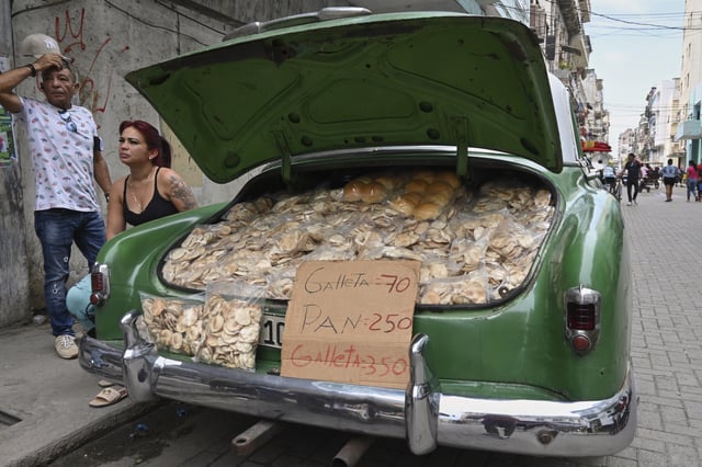 Vendors wait for customers next to the trunk of their American classic car stuffed with homemade crisps and bread, in Havana, Cuba, Tuesday, July 15, 2025. (AP Photo/Jorge Luis Baños)