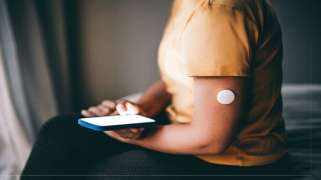 A user checks blood sugar data on a mobile app while wearing an arm-mounted glucose monitor.