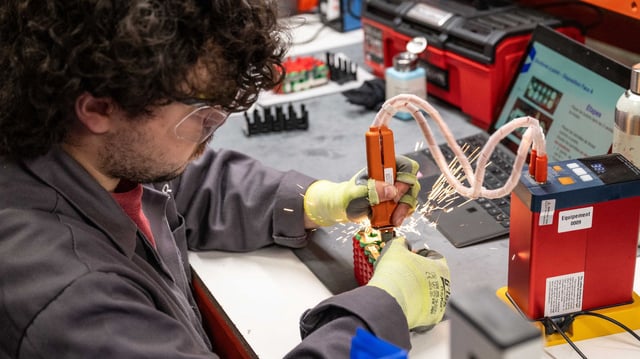 A researcher wearing safety gloves and goggles welds components on a battery module at a lab workstation. Sparks fly as the technician uses precision tools, highlighting the high-stakes environment of battery development. Representational image illustrating the kind of hands-on engineering behind advanced lithium metal battery prototypes, such as those now being equipped with built-in fire suppression technologies.